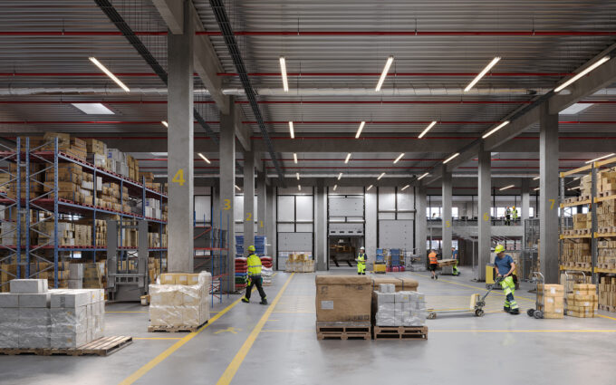 Expansive warehouse interior featuring tall racking, textured pallets, and dynamic lighting highlighting industrial finishes.
